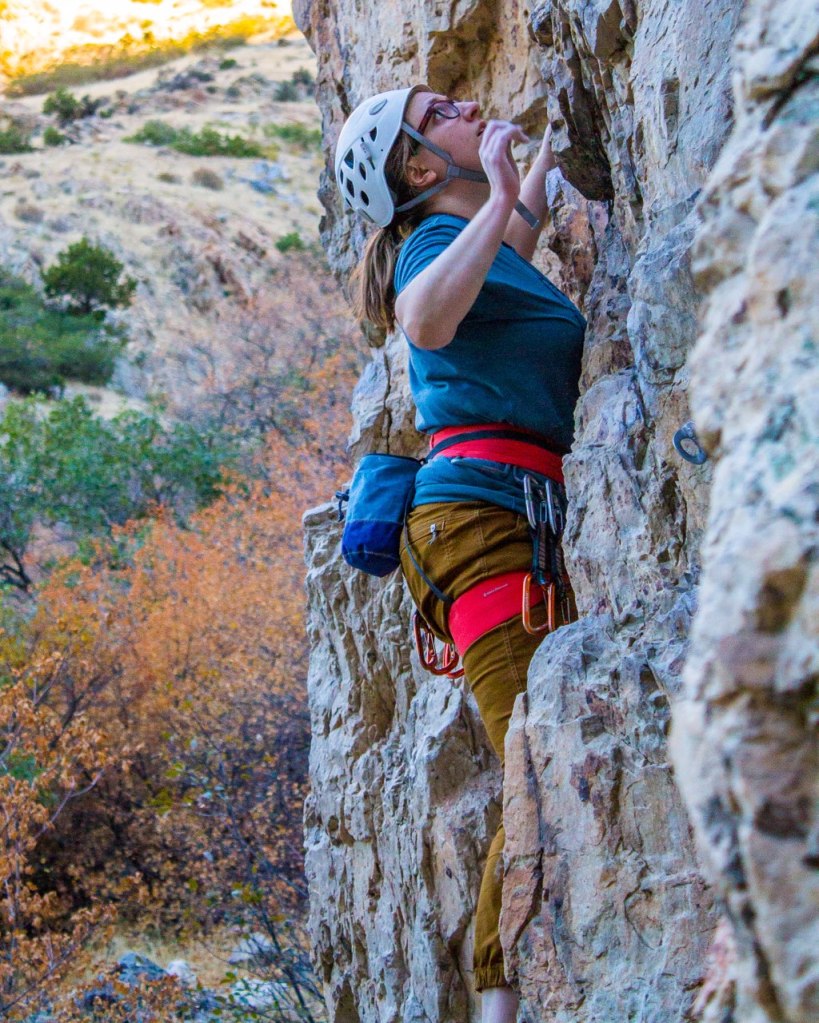 Anna lead climbing wearing an orange Petzl harness and a white Petzl helmet in Rock Canyon in Provo, Utah.